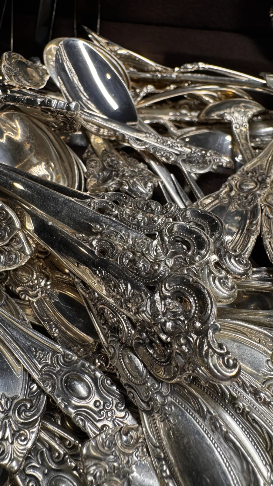 pile of ornate antique silver spoons and cutlery with intricate scroll patterns