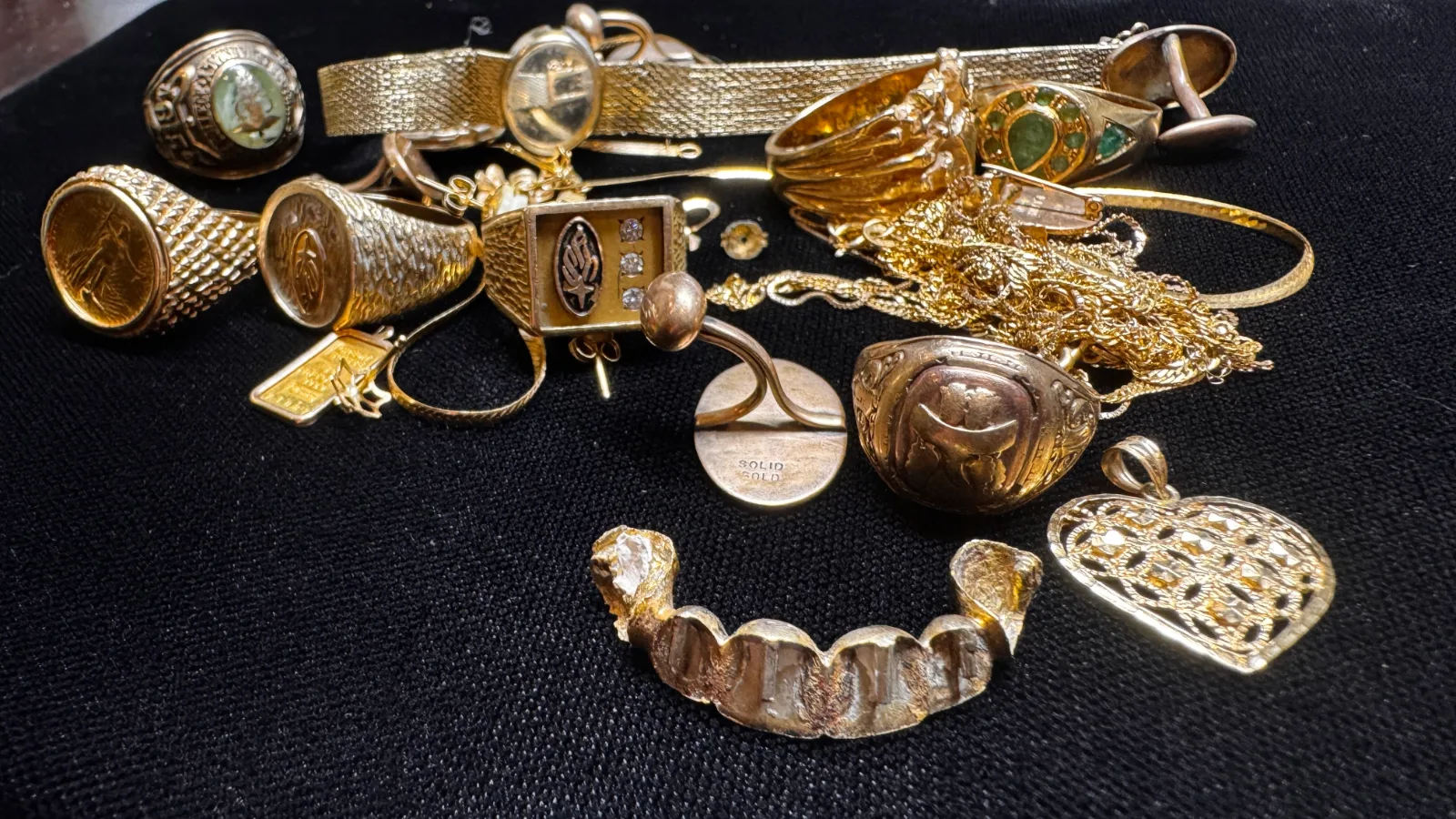 collection of gold jewelry rings and chains on a black surface