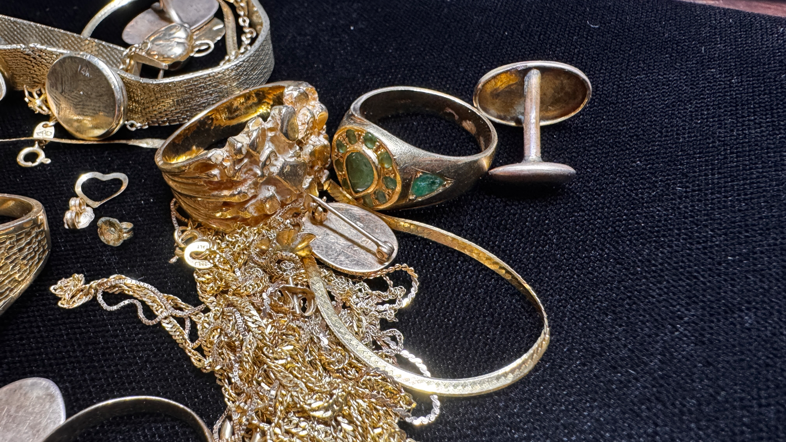 various gold rings and tangled necklaces scattered on black fabric