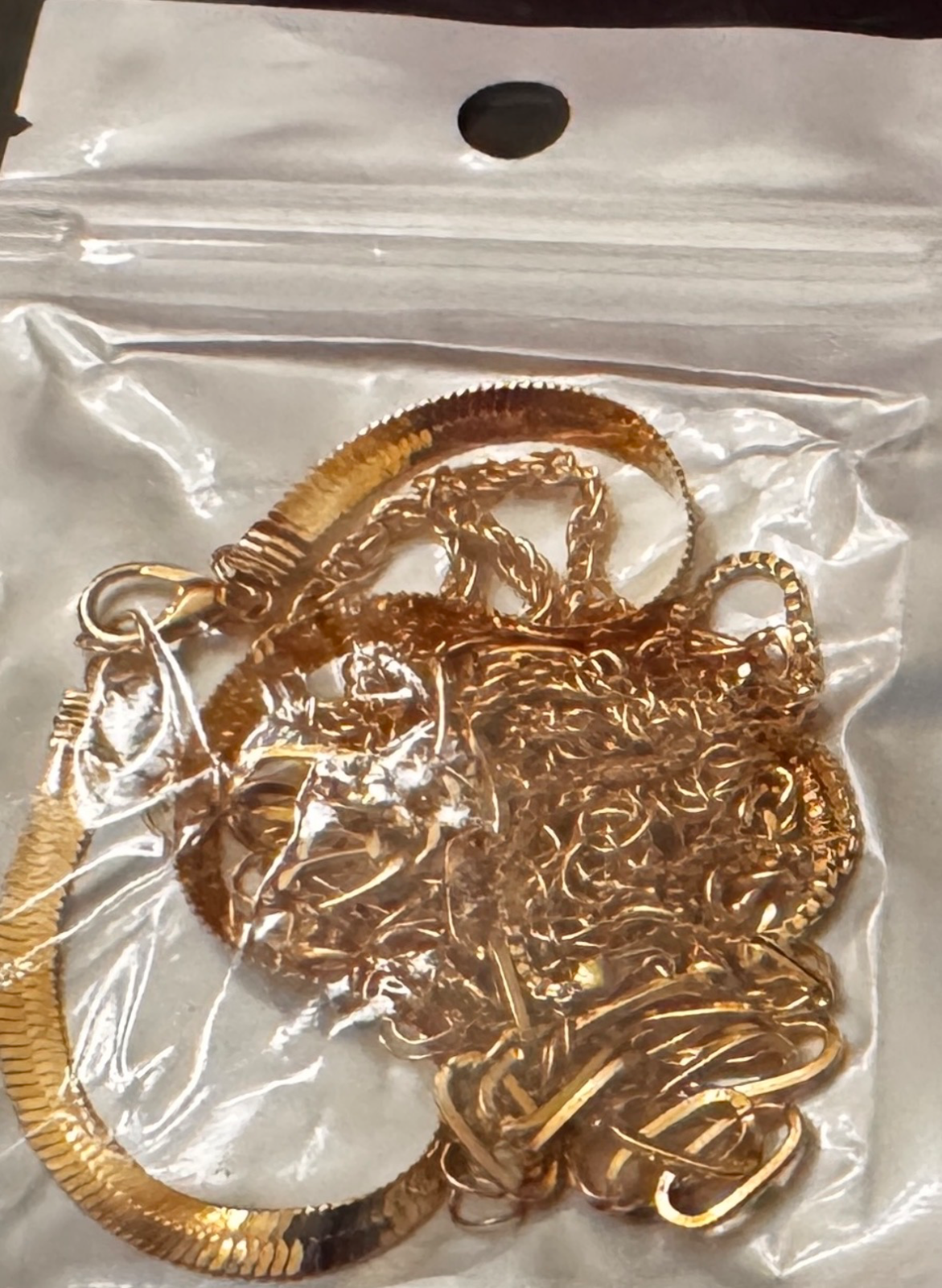 tangled gold herringbone and link chains inside a plastic bag