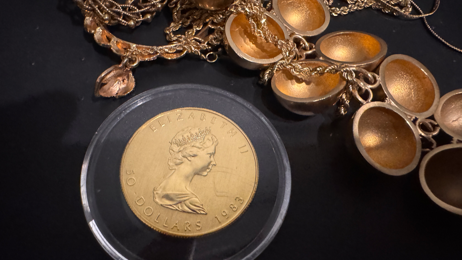 gold fifty dollar coin in plastic case beside gold jewelry