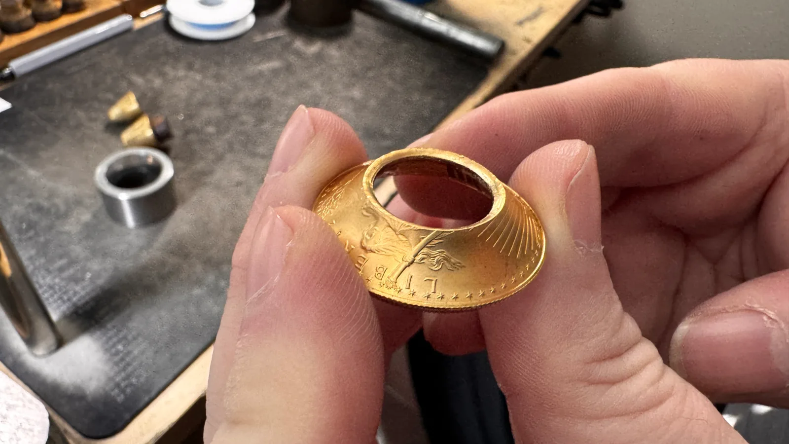 hands holding a curved gold coin being shaped into a ring