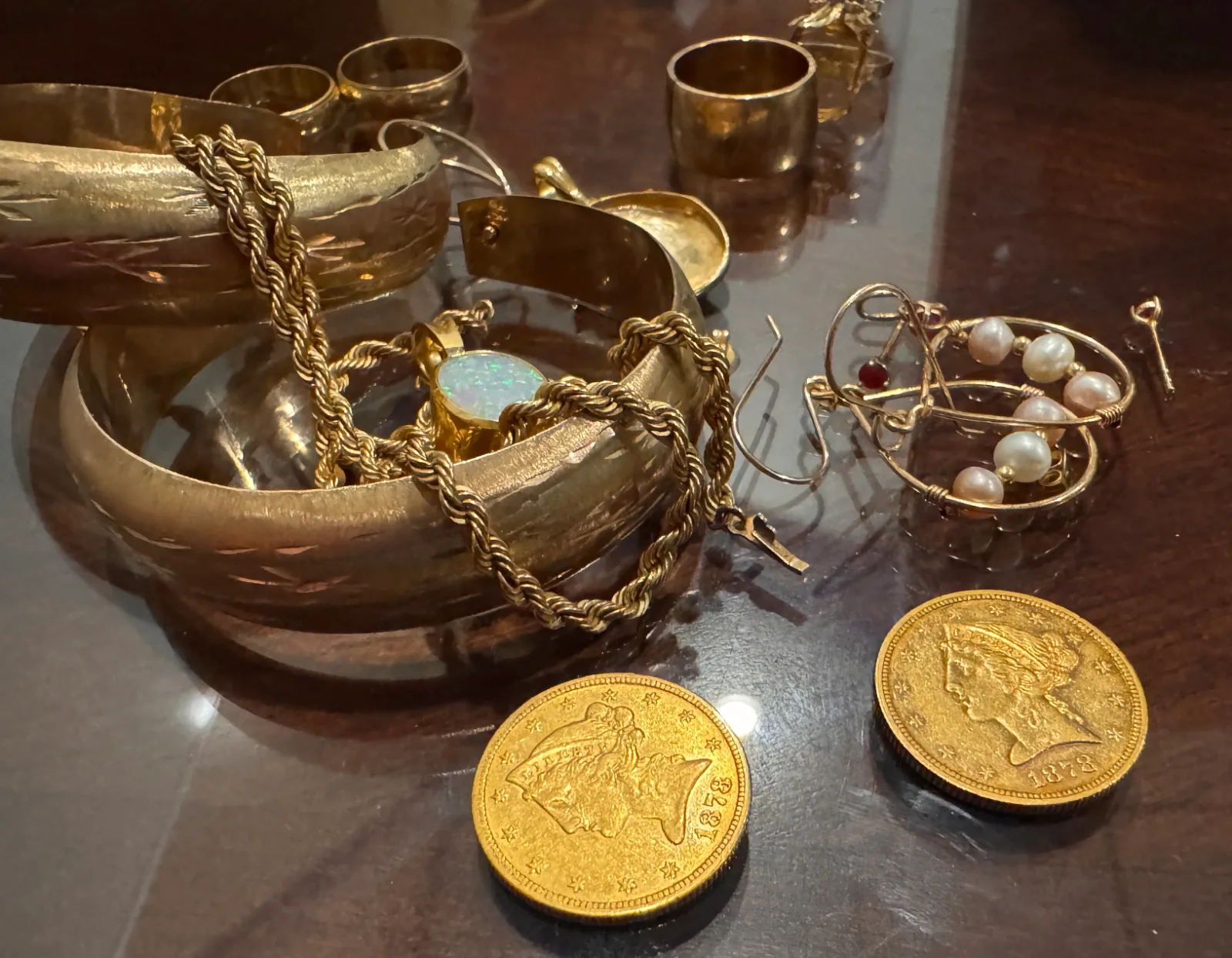various gold jewelry pieces bangles chains and coins on a dark surface