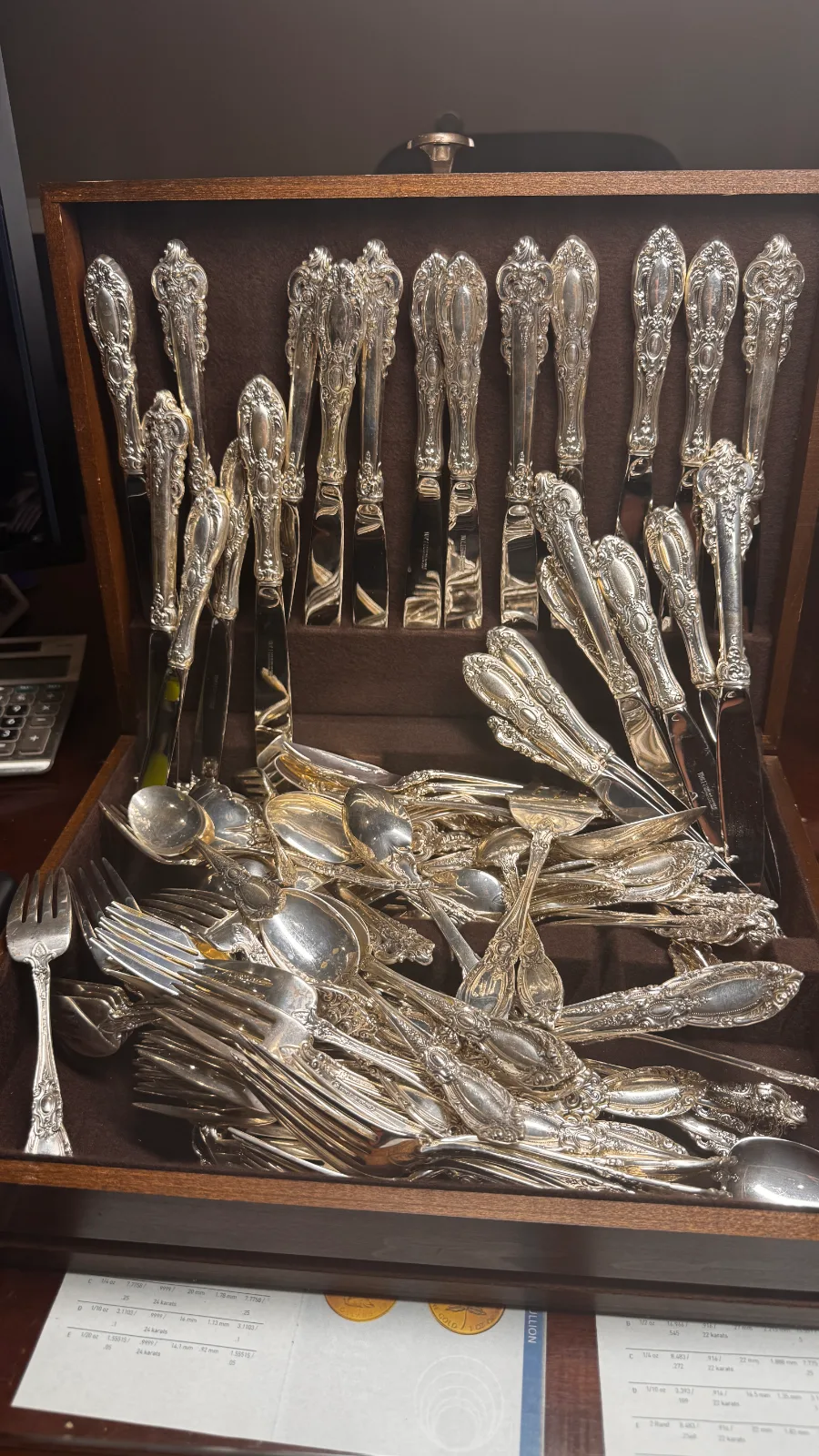 ornate silver cutlery set organized inside a dark wooden chest