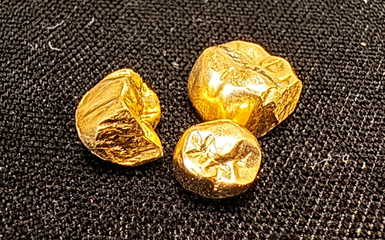 three small raw gold nuggets on a black textured surface